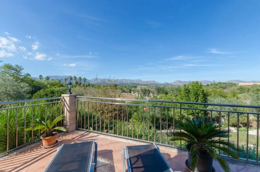 A sunny terrace overlooks green vegetation and distant hills.