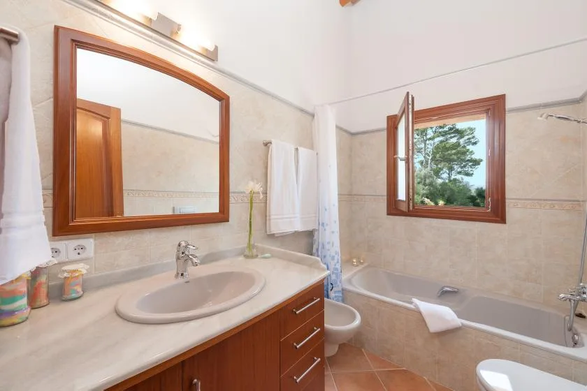 A bathroom with a sink, mirror, and bathtub beside an open window.