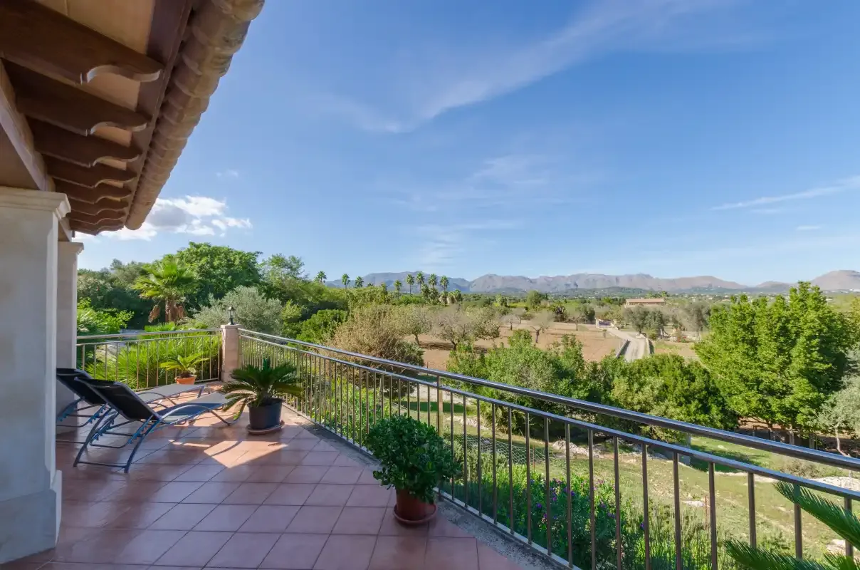 A tiled balcony with seating overlooks green fields and distant hills.