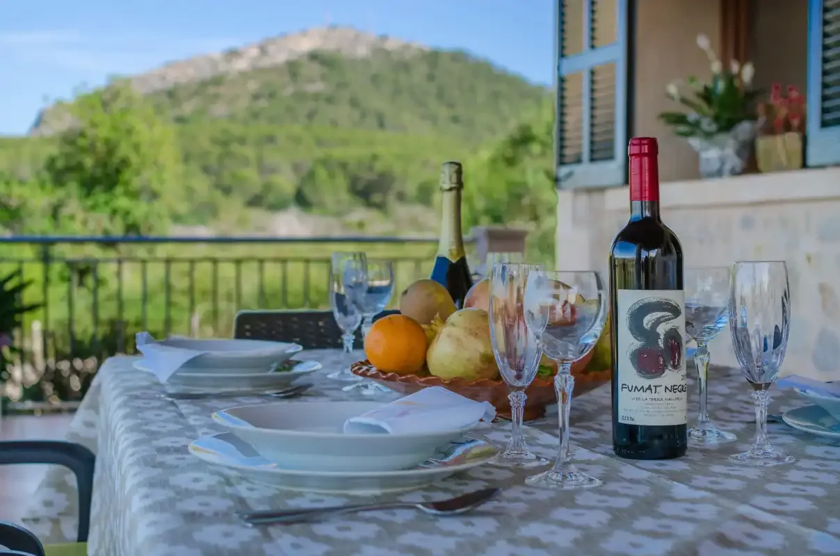 A dining table is set with dishes and wine beside an outdoor view of green hills.