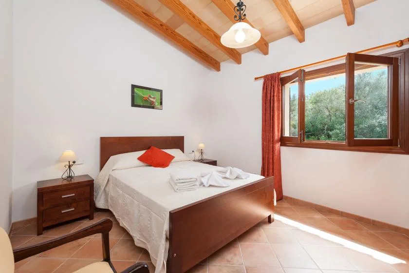 A bedroom with a neatly made bed beside an open window.