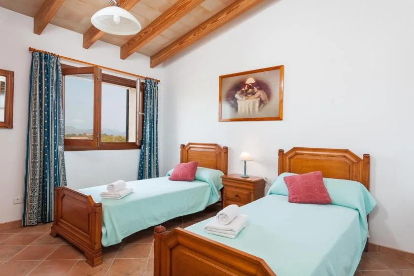 A twin bedroom with wooden beds, turquoise bedding, and a window with curtains.