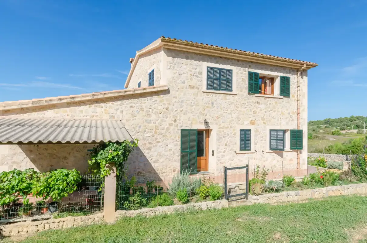A stone house with green shutters stands beside a small garden.
