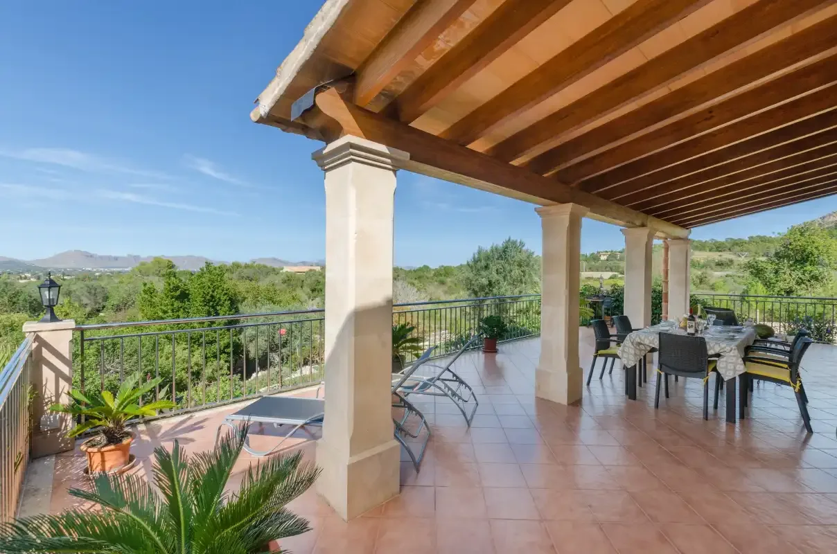 A covered terrace with outdoor seating overlooks a green landscape.