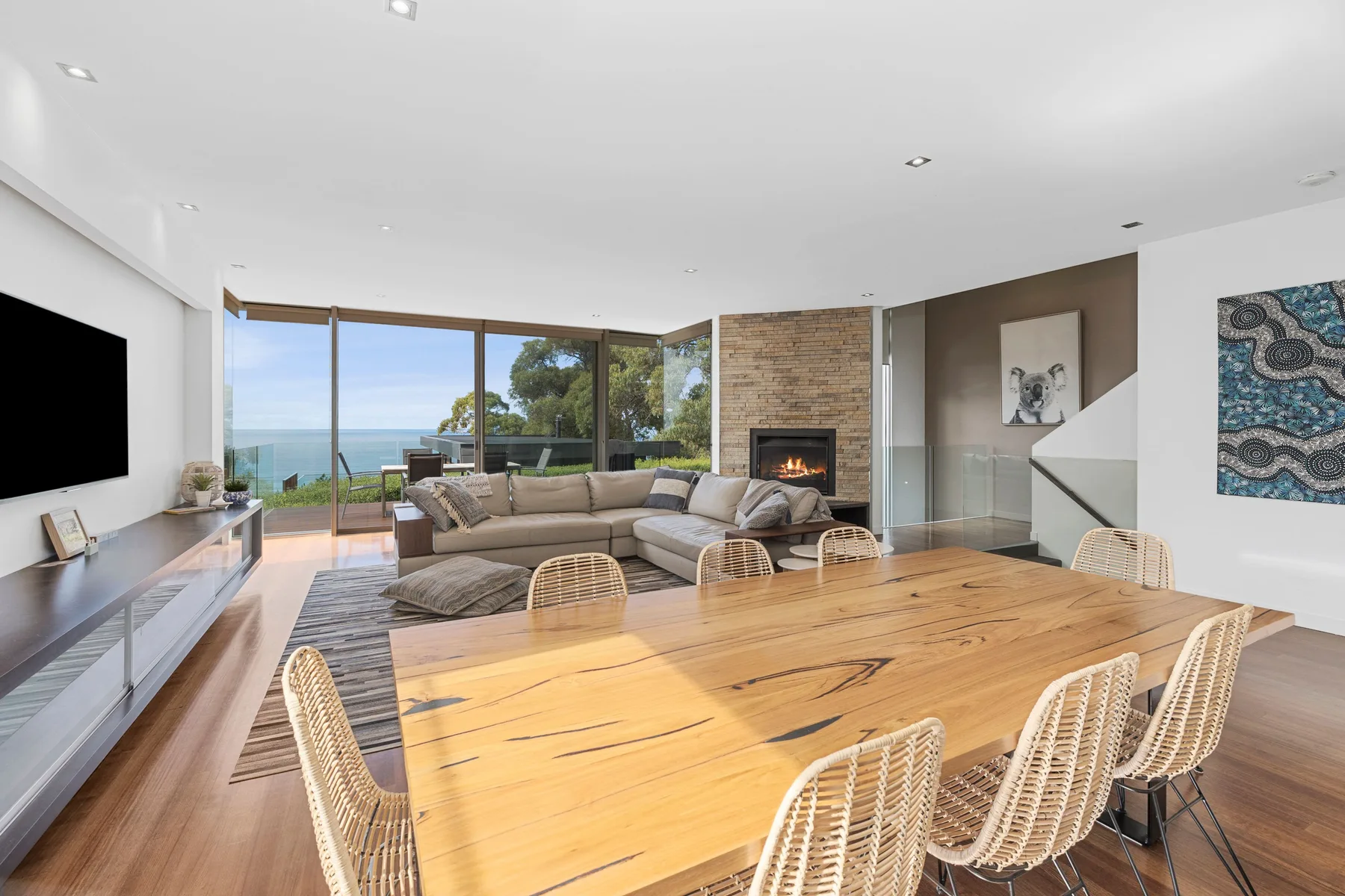 Sala de estar y comedor con una gran mesa de madera y vistas al mar a través de puertas de vidrio.