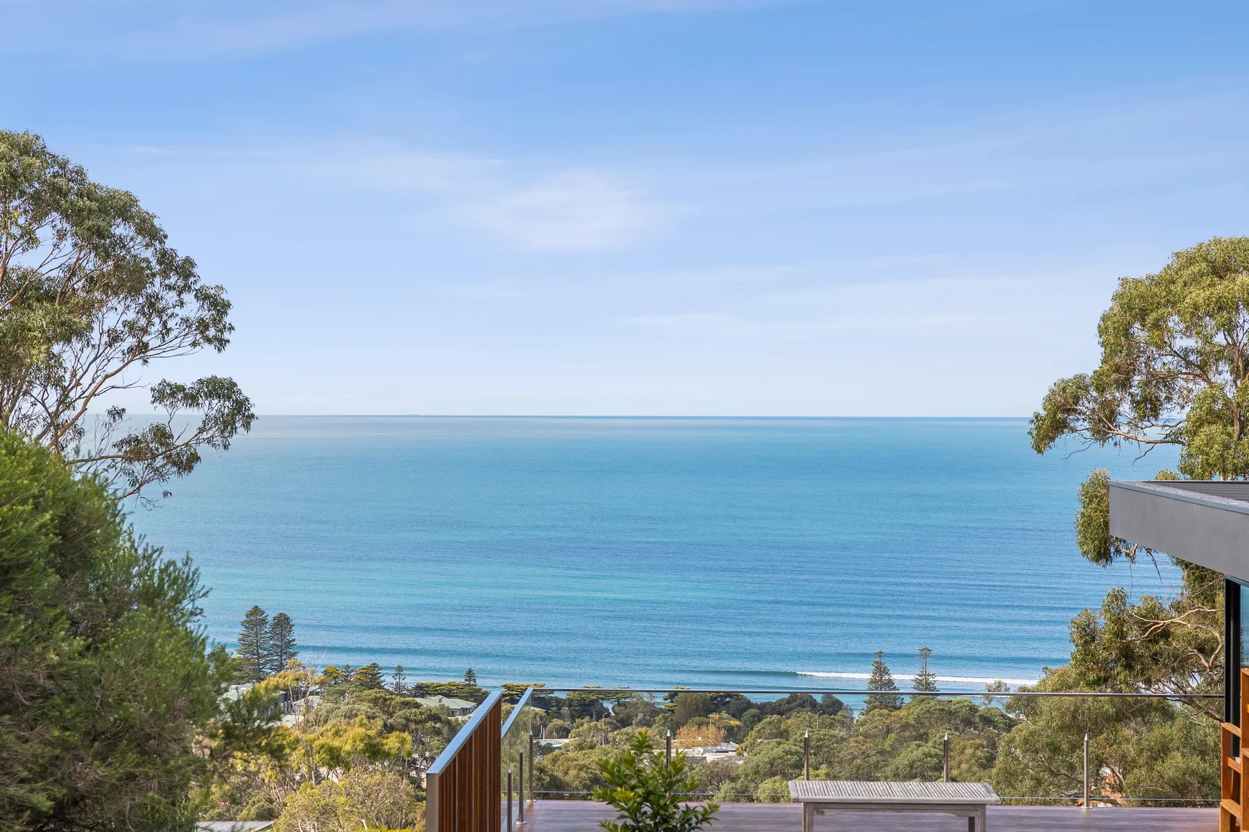 Ocean view from an elevated outdoor deck framed by trees.