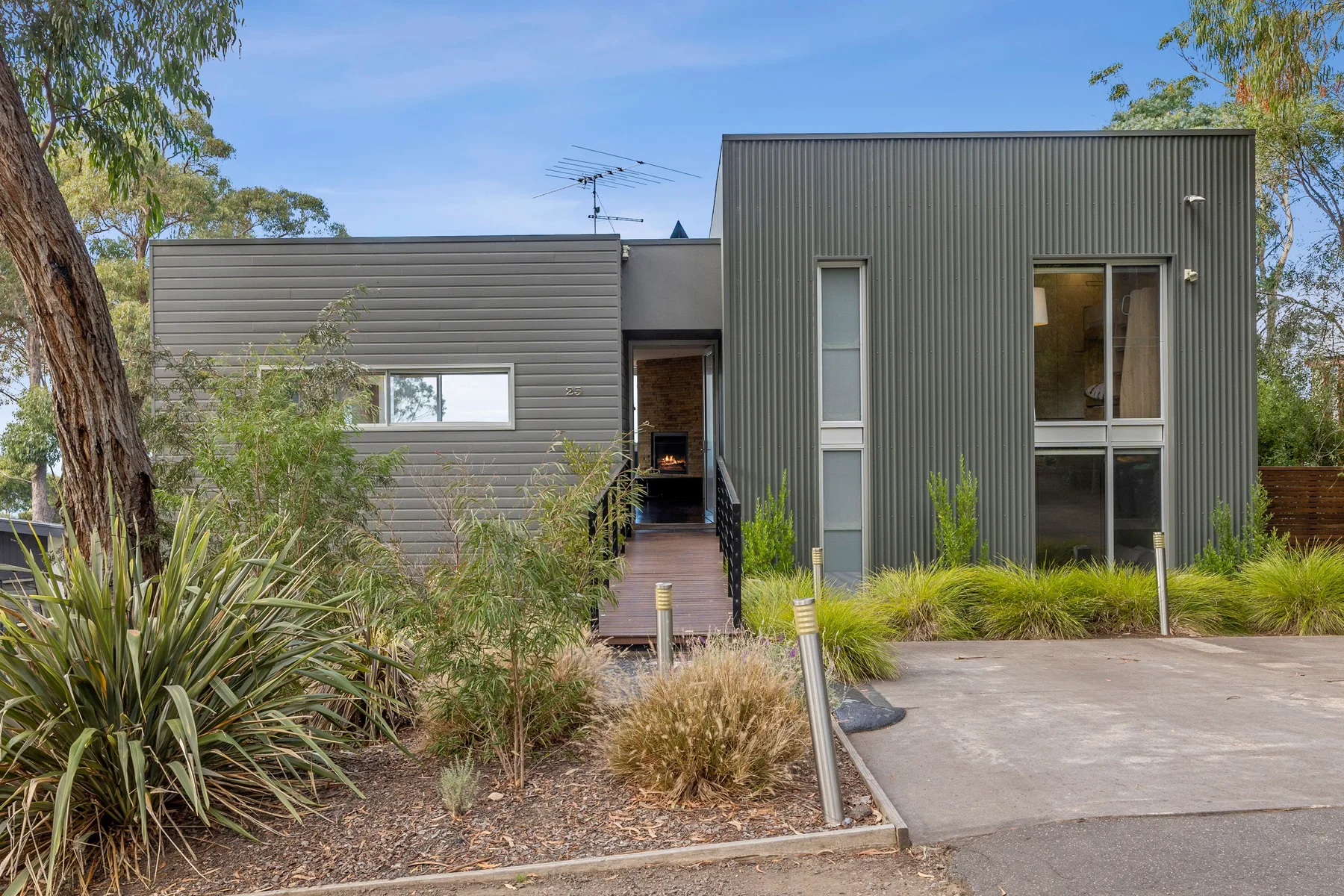 A modern house stands beside landscaped garden beds and a paved driveway.