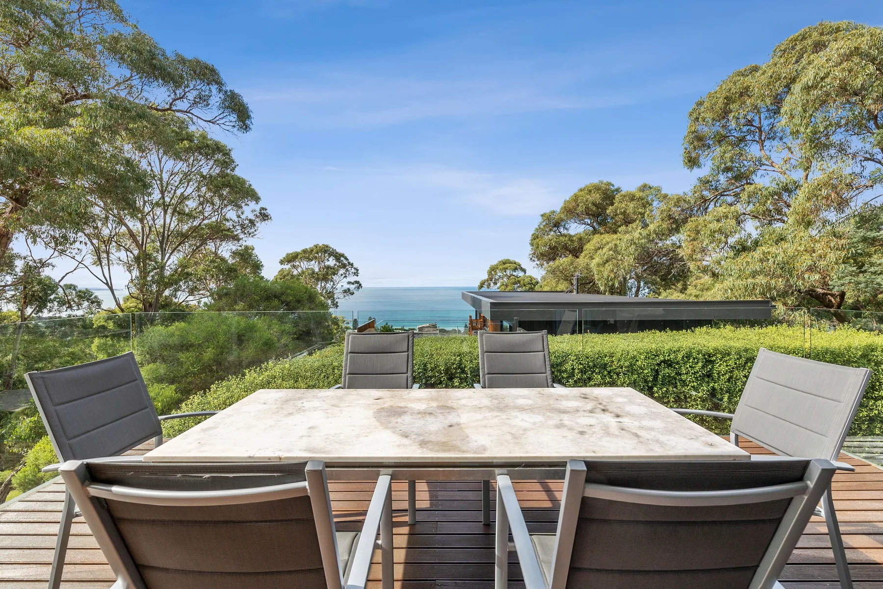 An outdoor dining area overlooks the ocean, with trees surrounding the deck.