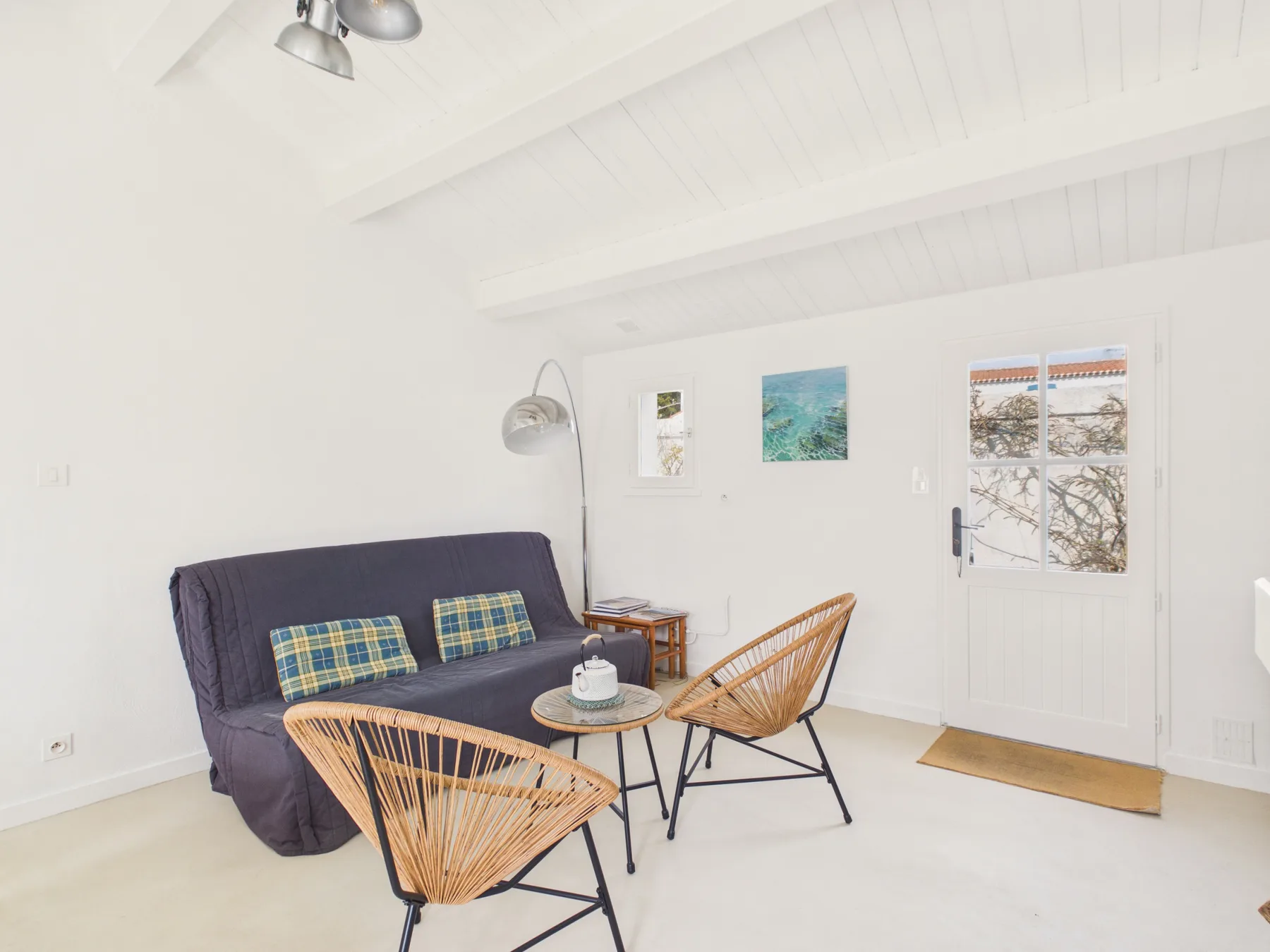 A bright sitting area has a dark sofa, woven chairs, and a door with a window.