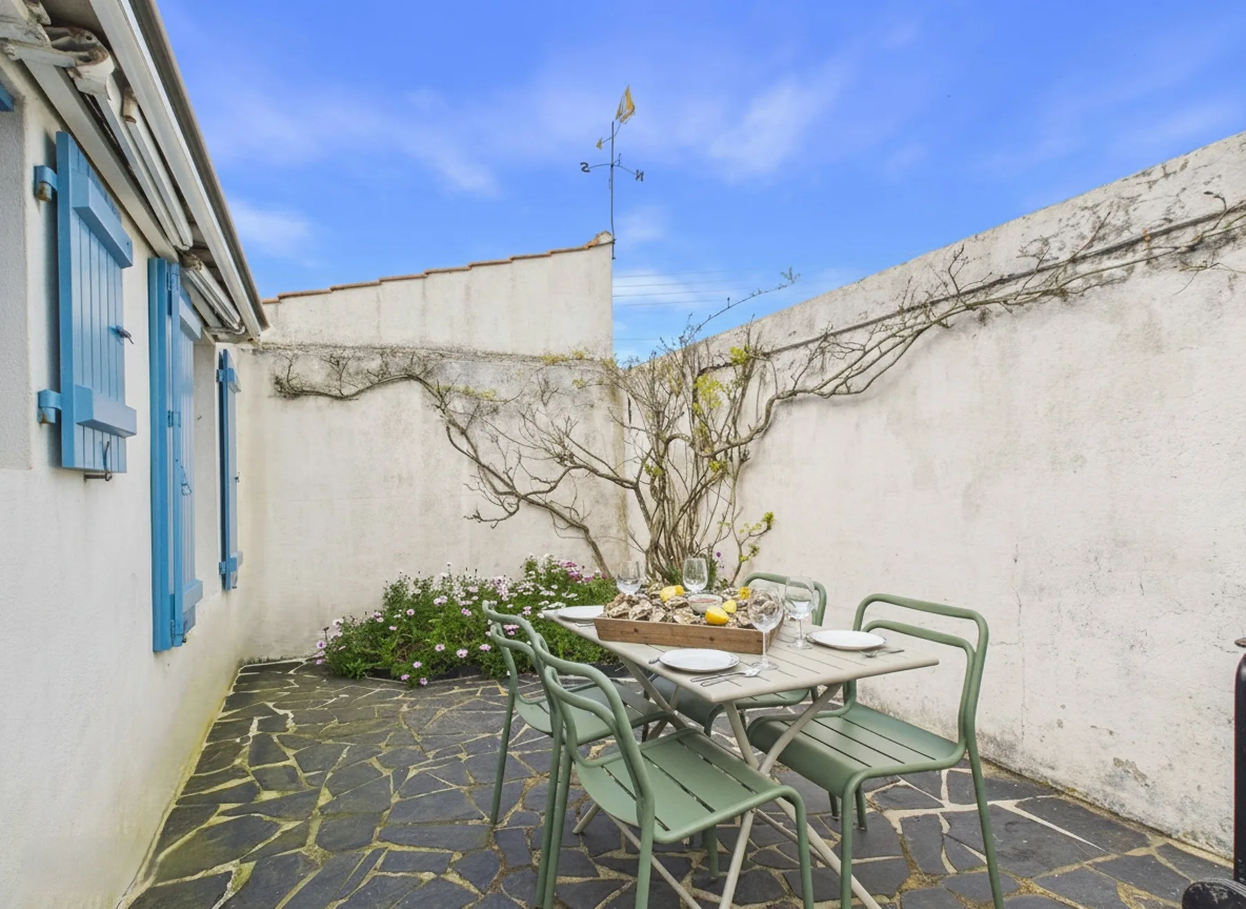 A small paved courtyard with outdoor seating and a table beside white walls.