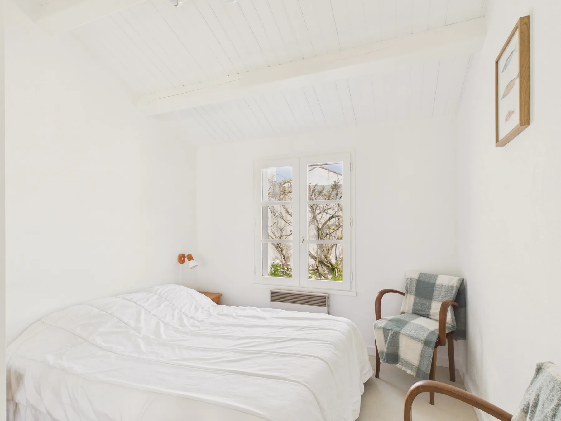 A bright bedroom with a bed and a window overlooking trees.