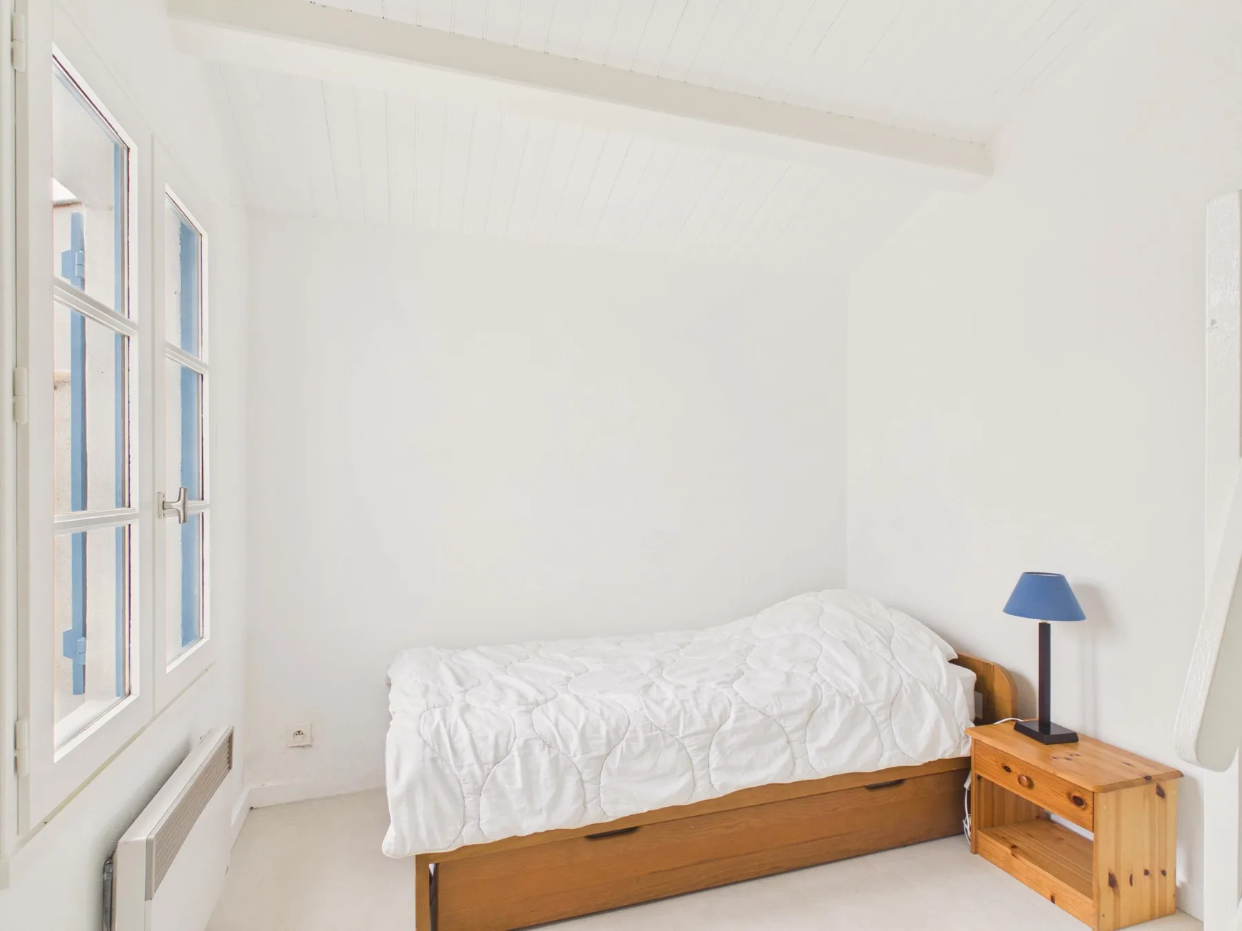 A bedroom with a single bed and a wooden bedside table.