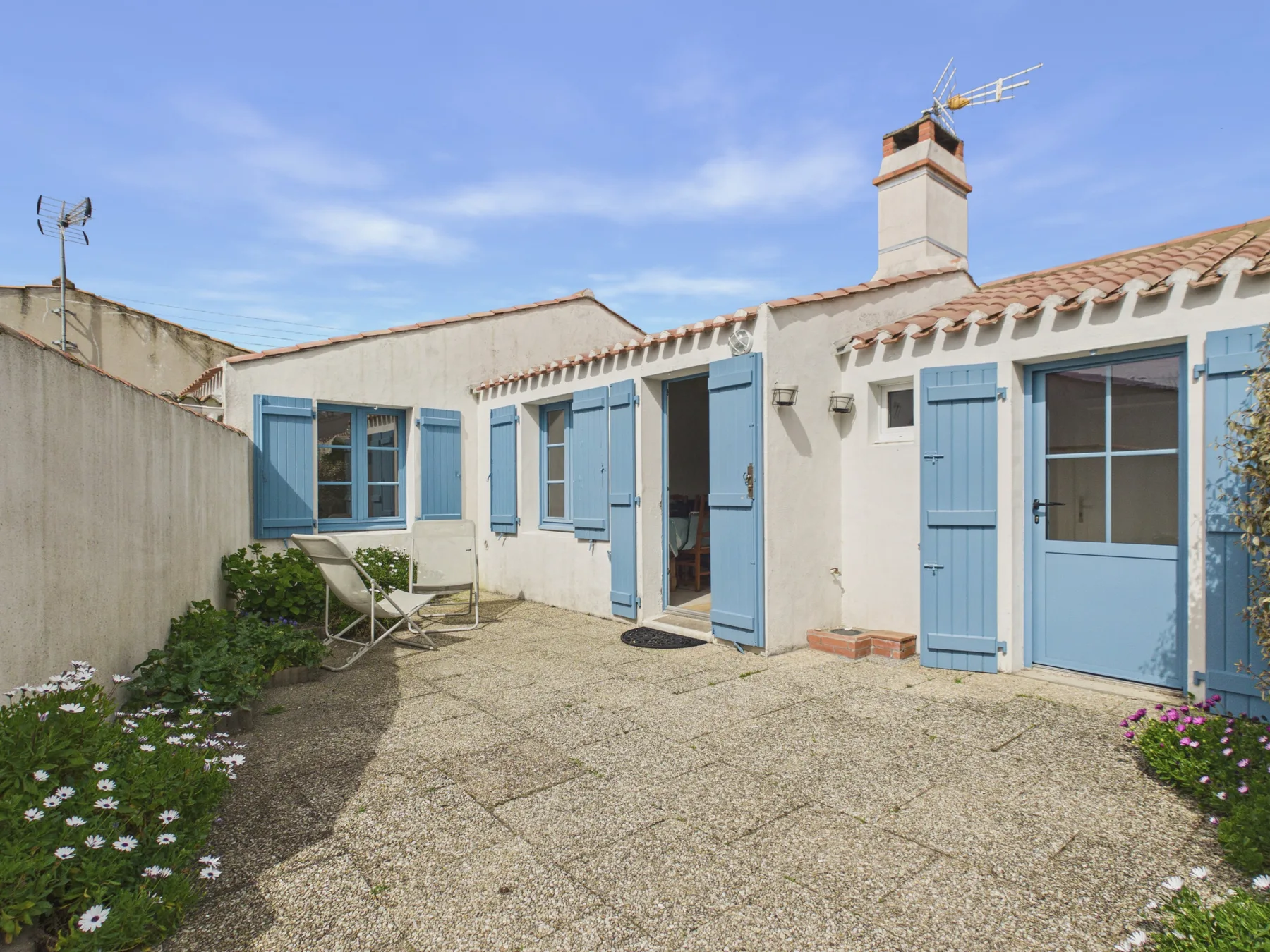 A sunny paved courtyard with blue shutters and a small seating area.