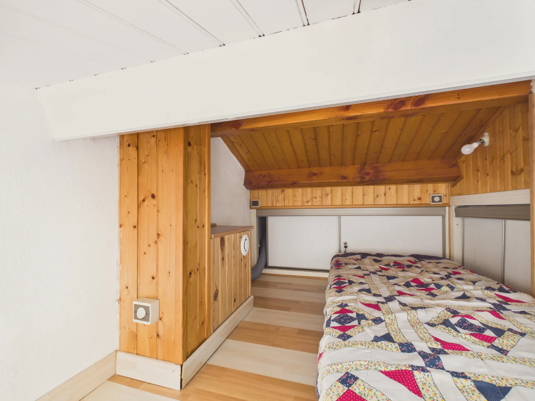 A bedroom with a bed beneath a wooden ceiling.