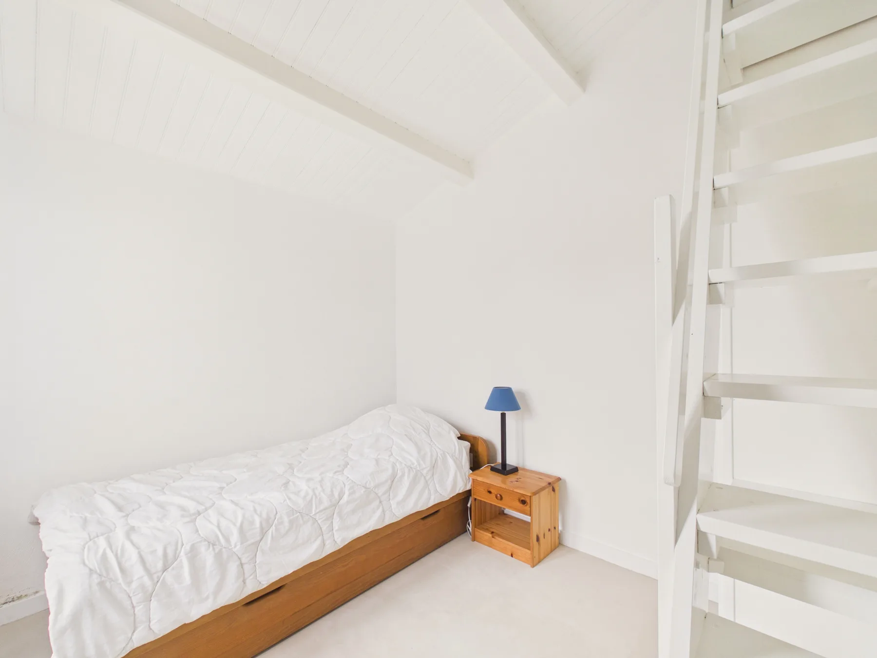 A bright bedroom with a single bed and a small bedside table.