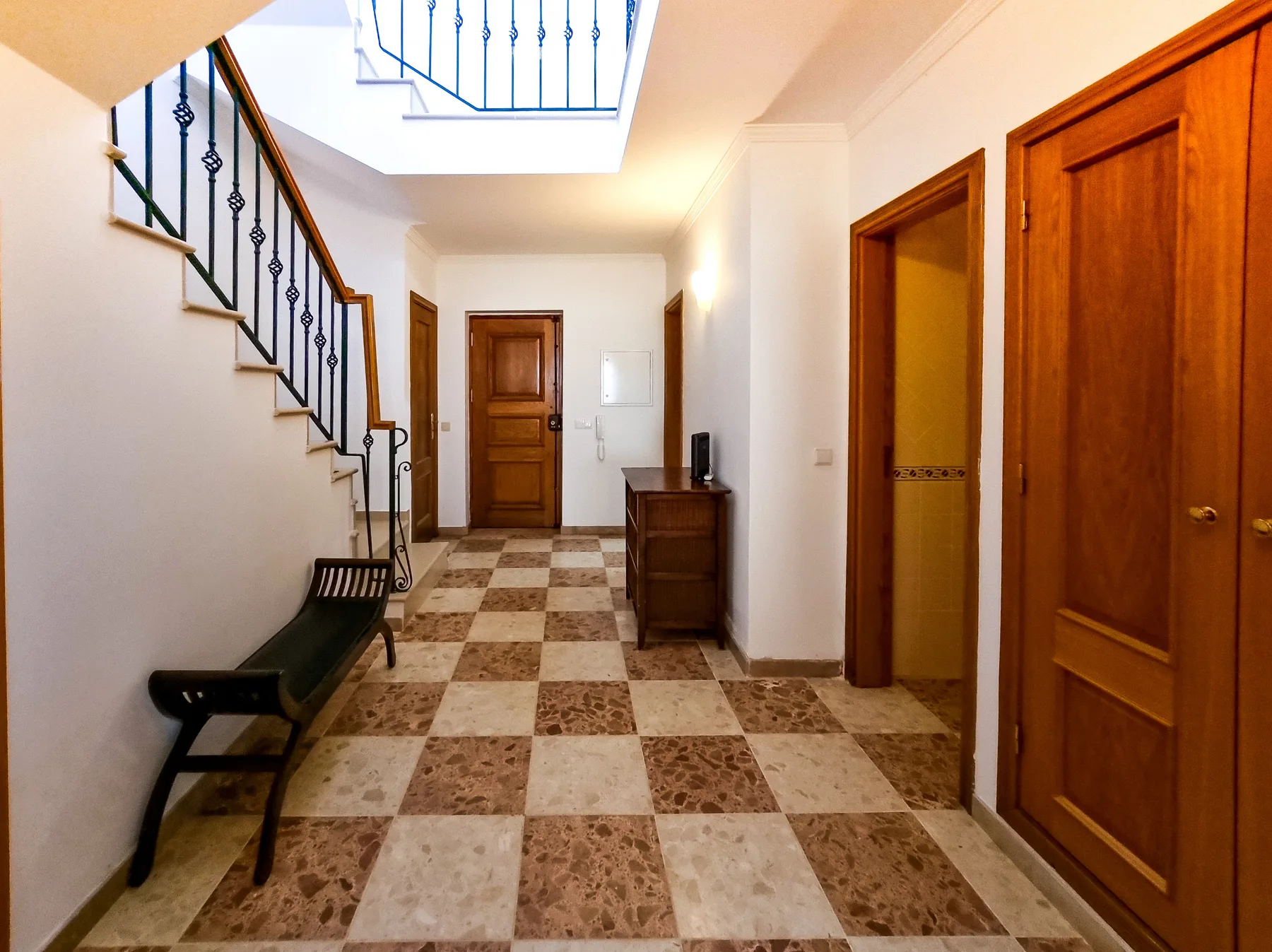 Un pasillo de baldosas con puertas de madera, una escalera y un banco.