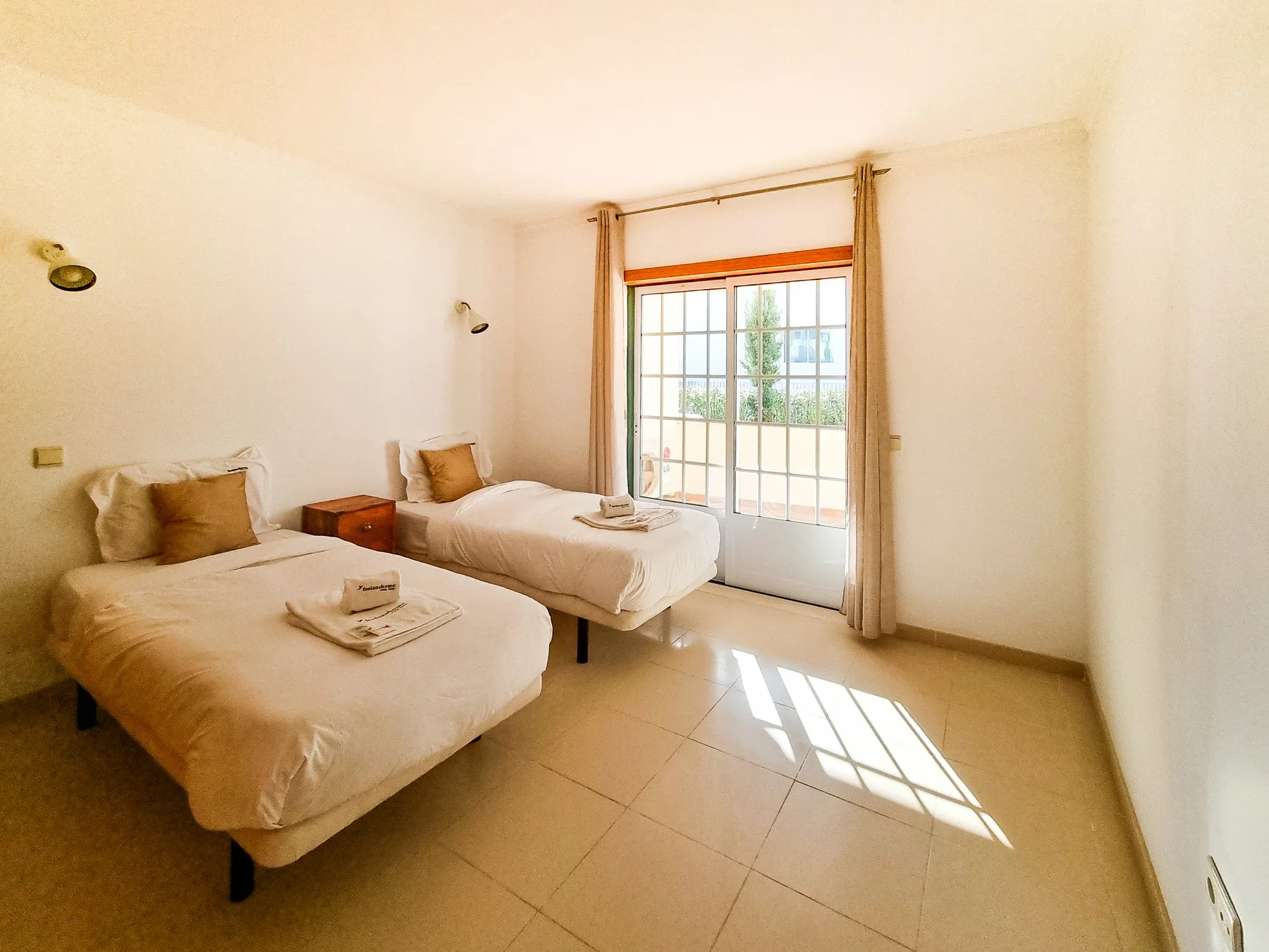 Un dormitorio luminoso con dos camas junto a una puerta grande de vidrio.