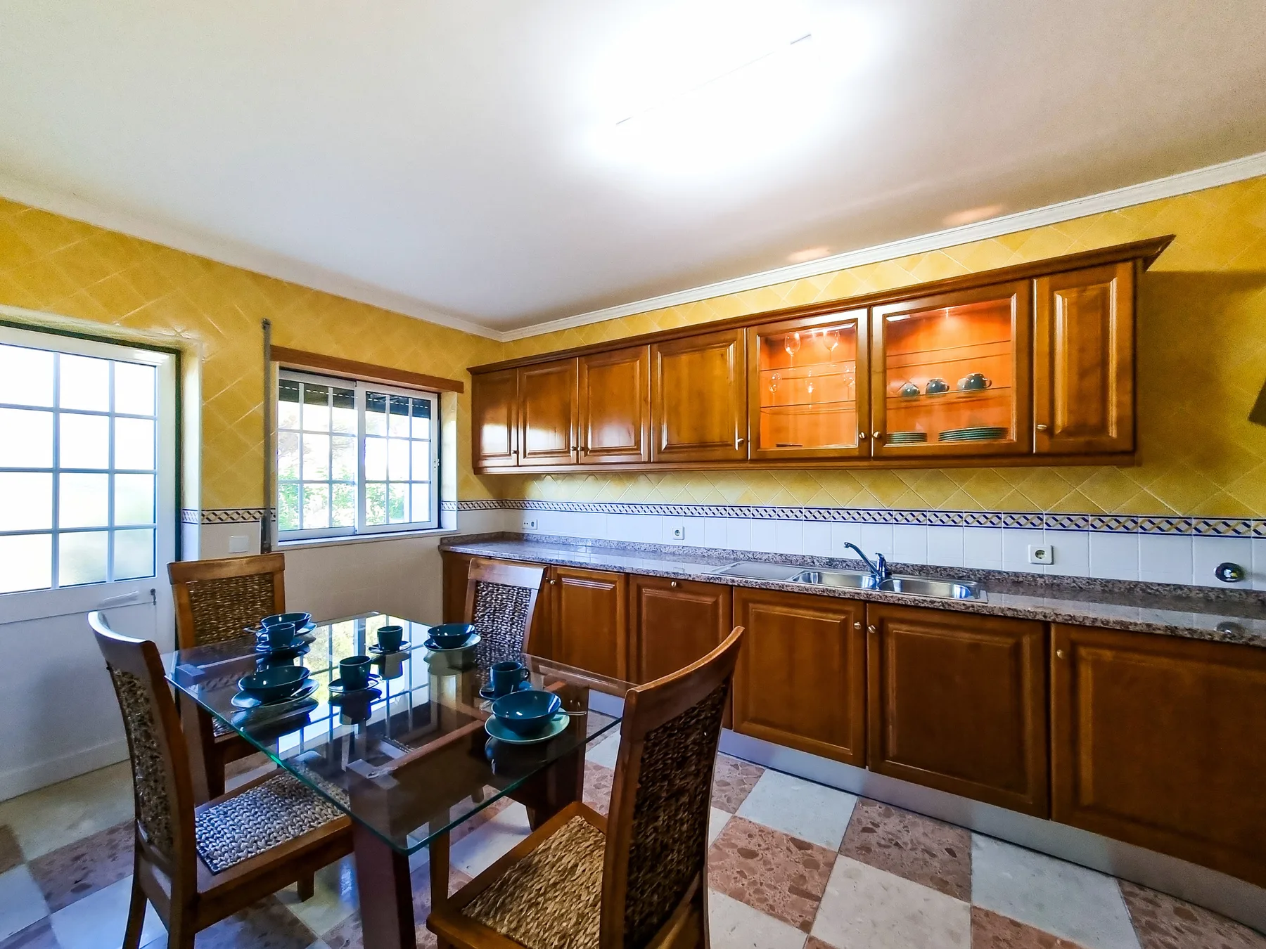 Cocina y comedor con gabinetes de madera y una mesa de comedor de vidrio.