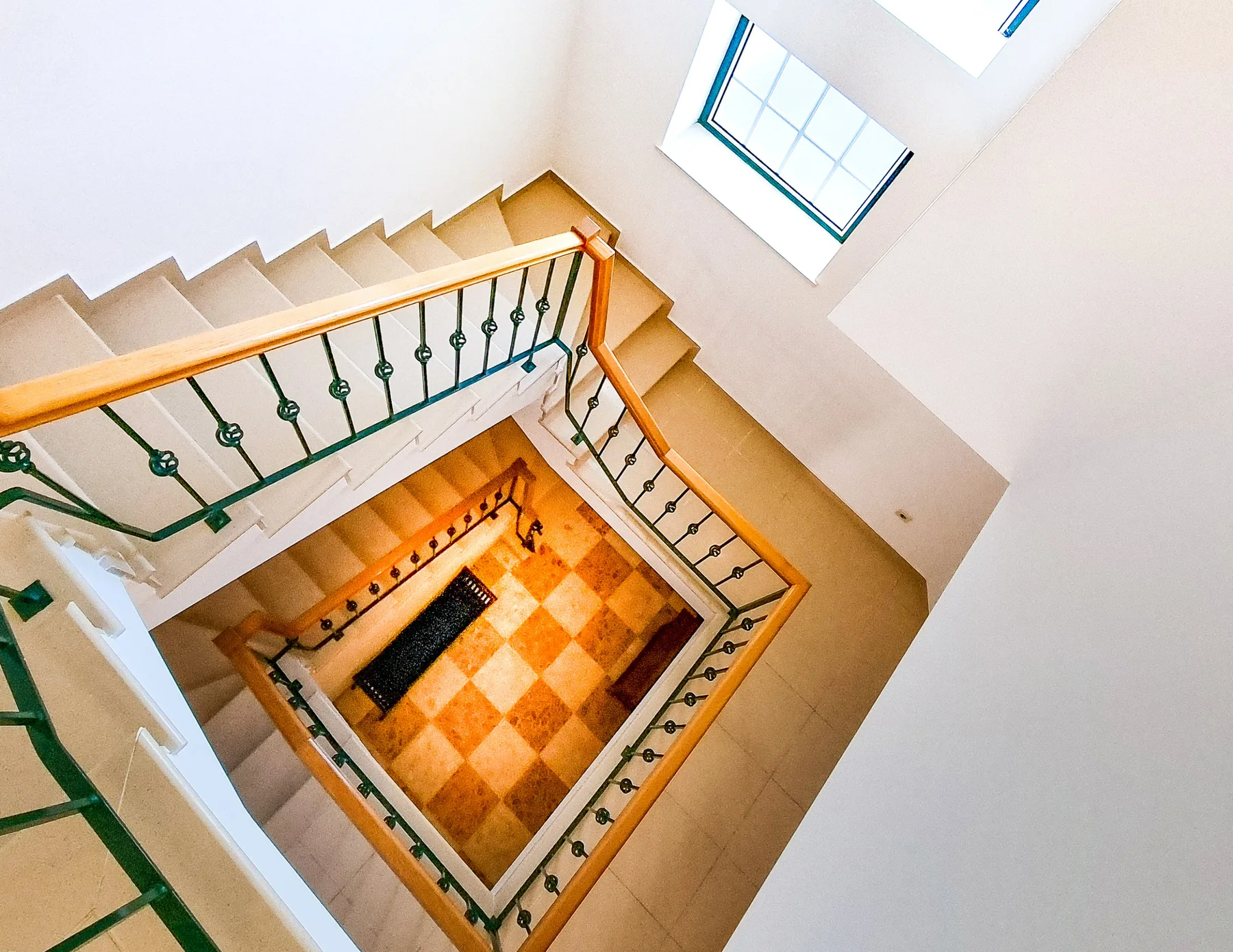 A staircase with decorative railings overlooks a tiled landing and a window.