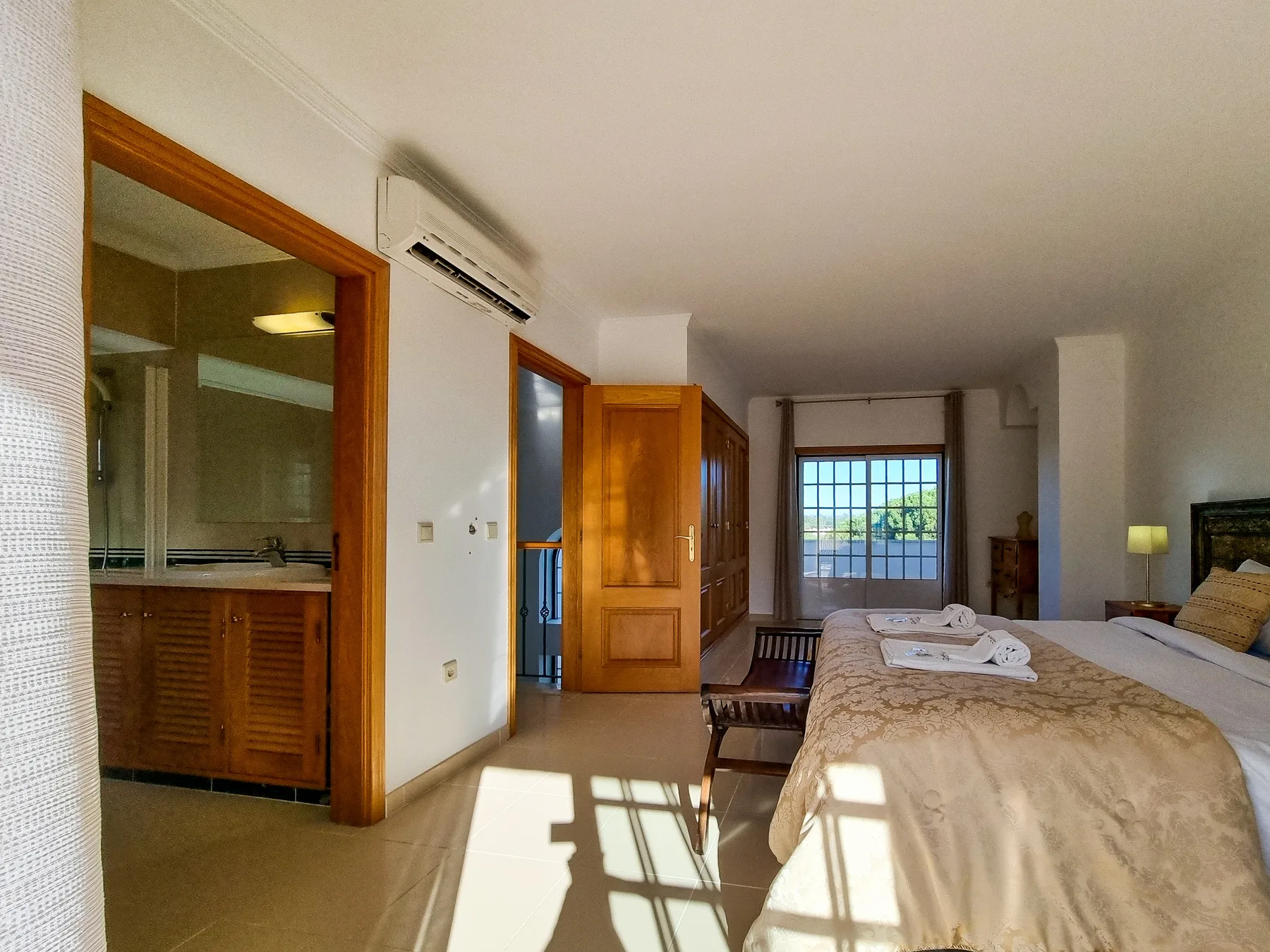 Un dormitorio con una cama grande, muebles de madera y una ventana con vistas a la vegetación.