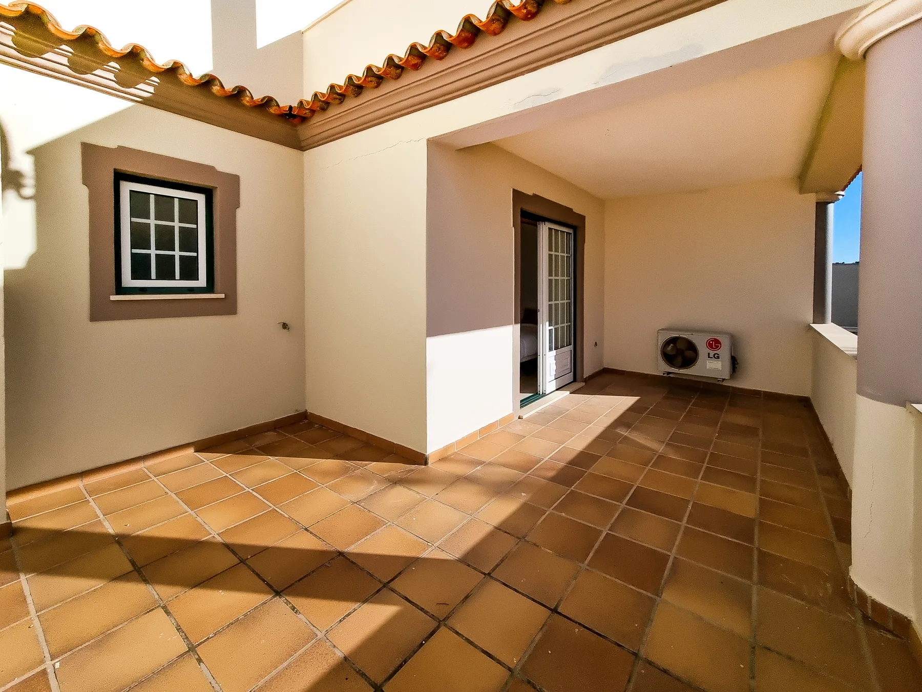 Un patio cubierto con suelo de baldosas, una ventana, una puerta y aire acondicionado en la pared.