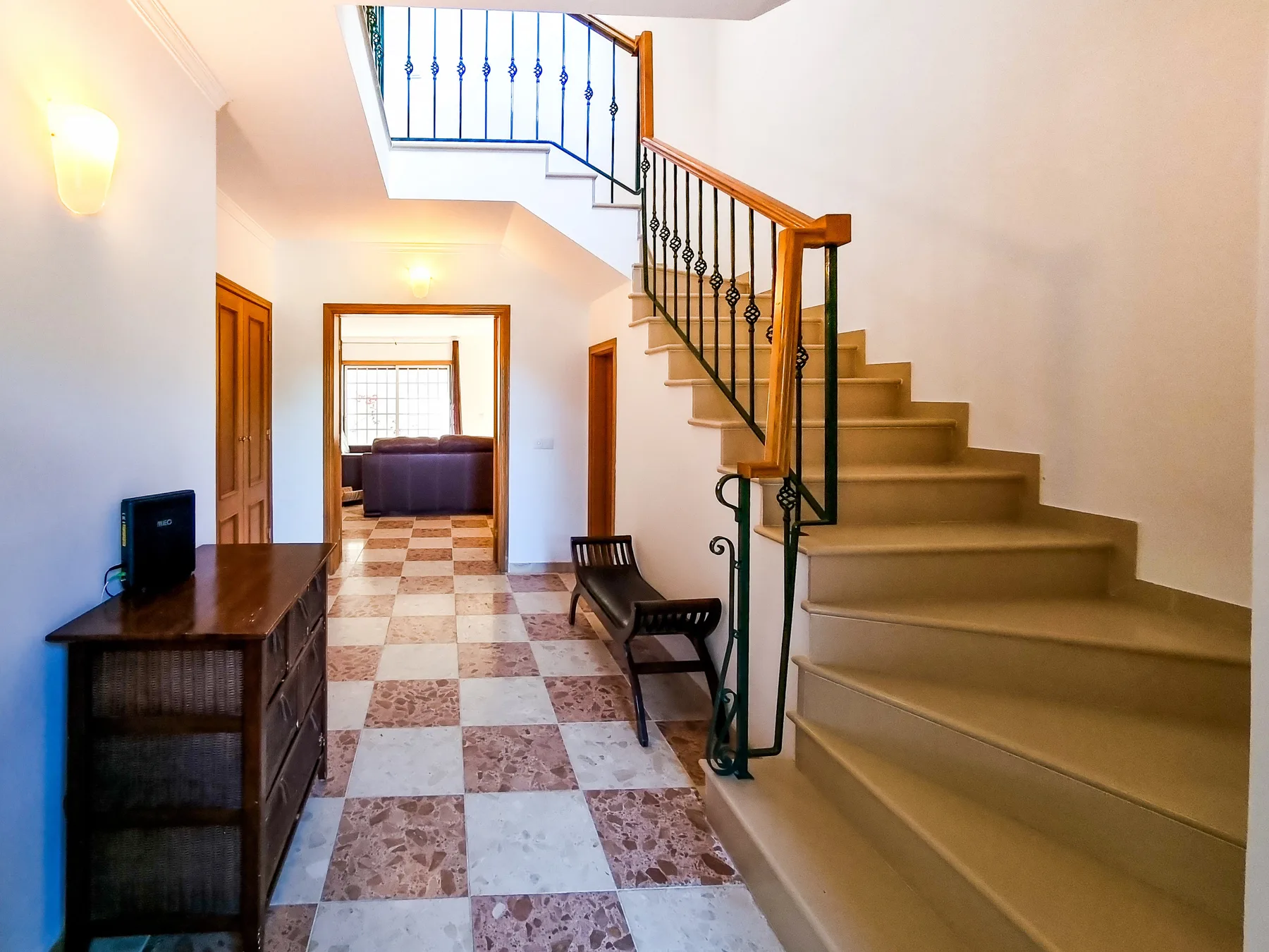 Una escalera interior con barandilla oscura sube sobre un pasillo de baldosas.
