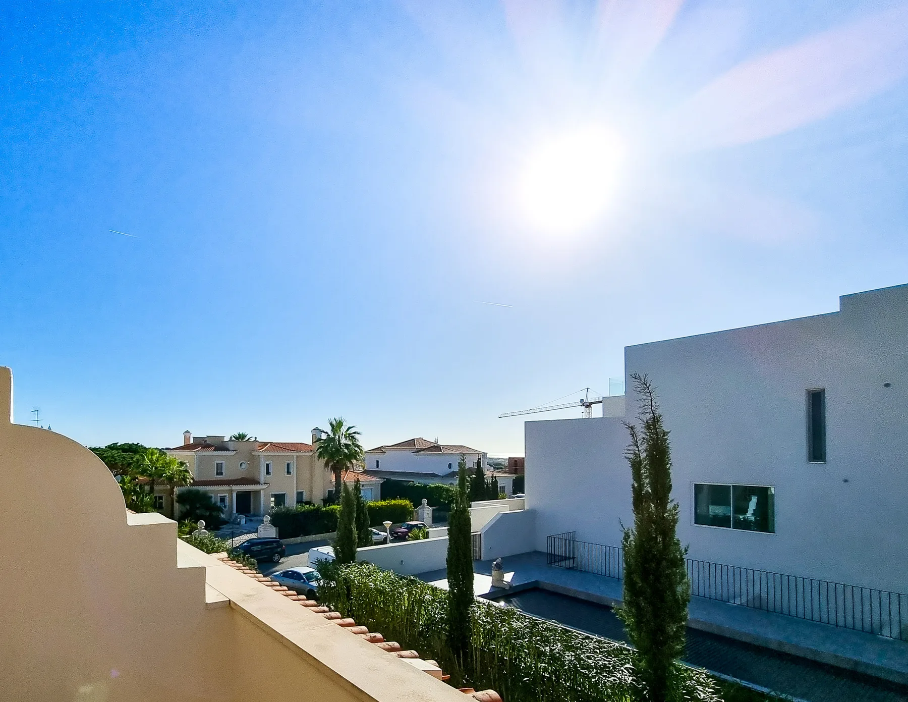Se ven edificios residenciales y árboles bajo el sol, tras un muro curvo de balcón.