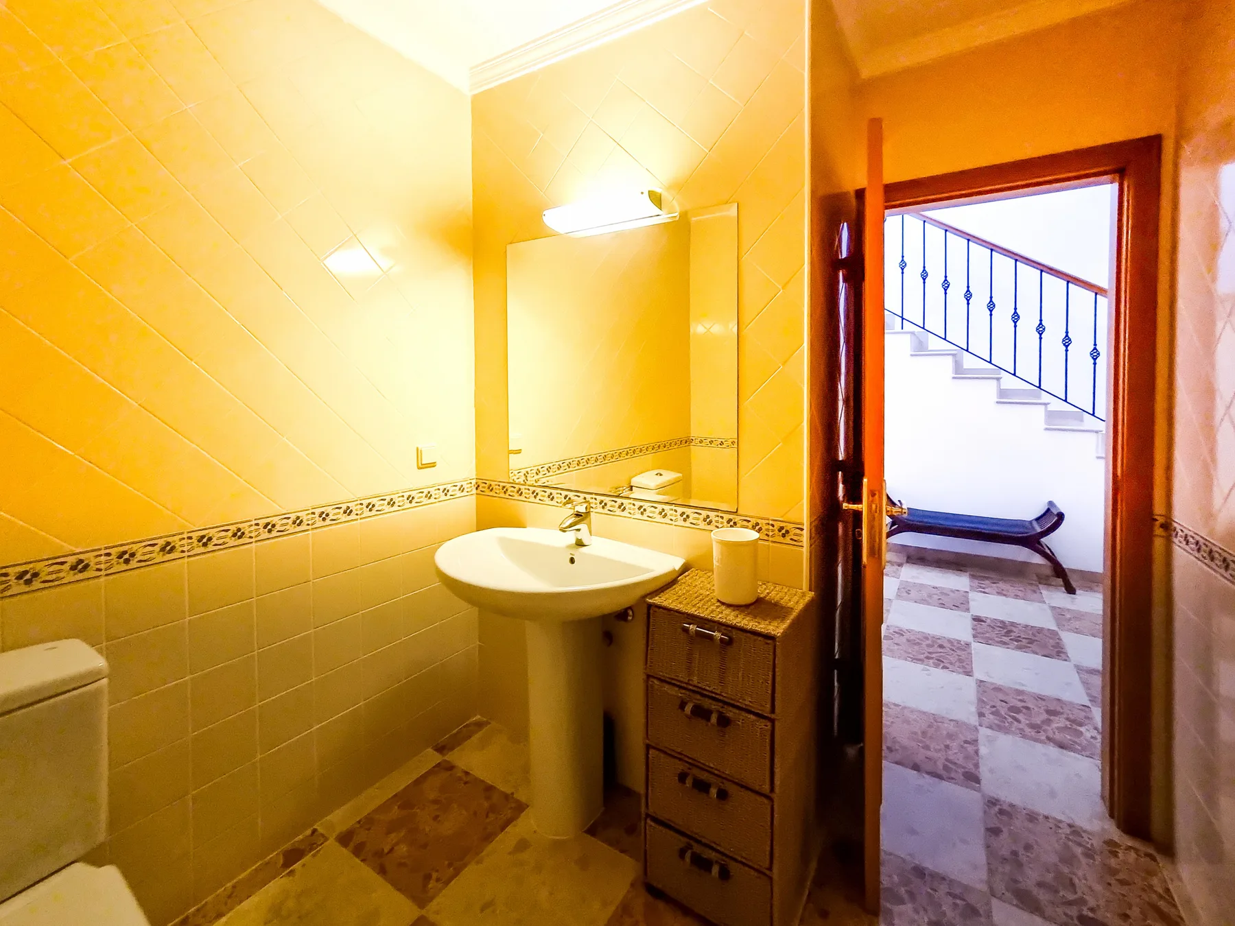 Baño alicatado con lavabo de pedestal y una puerta abierta hacia una escalera.