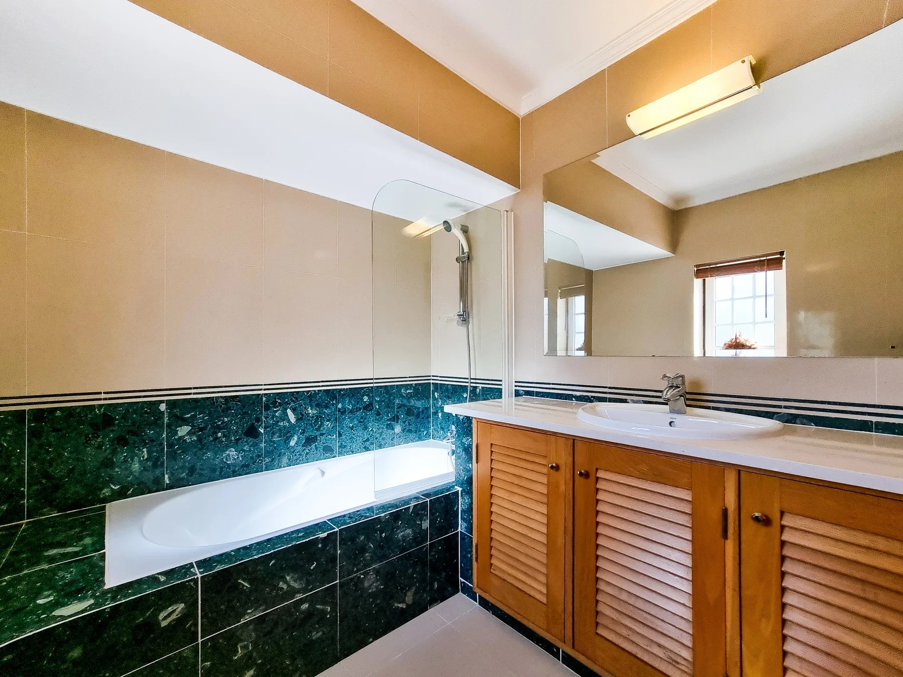 Un baño alicatado con bañera, mampara de vidrio y mueble de madera.