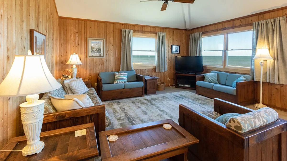 A wood-paneled living room with seating, a coffee table, and ocean views through the windows.