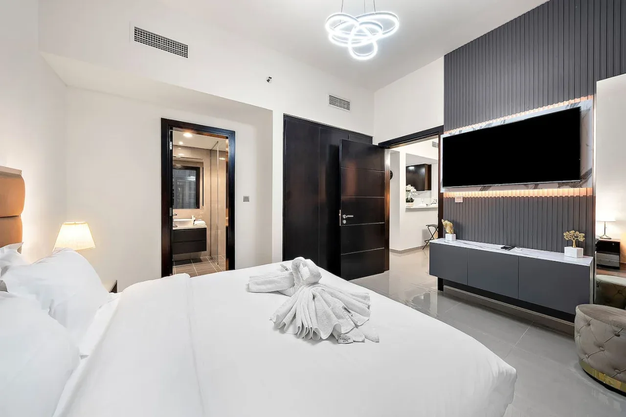 A bright bedroom with white bedding and a television mounted on the wall.