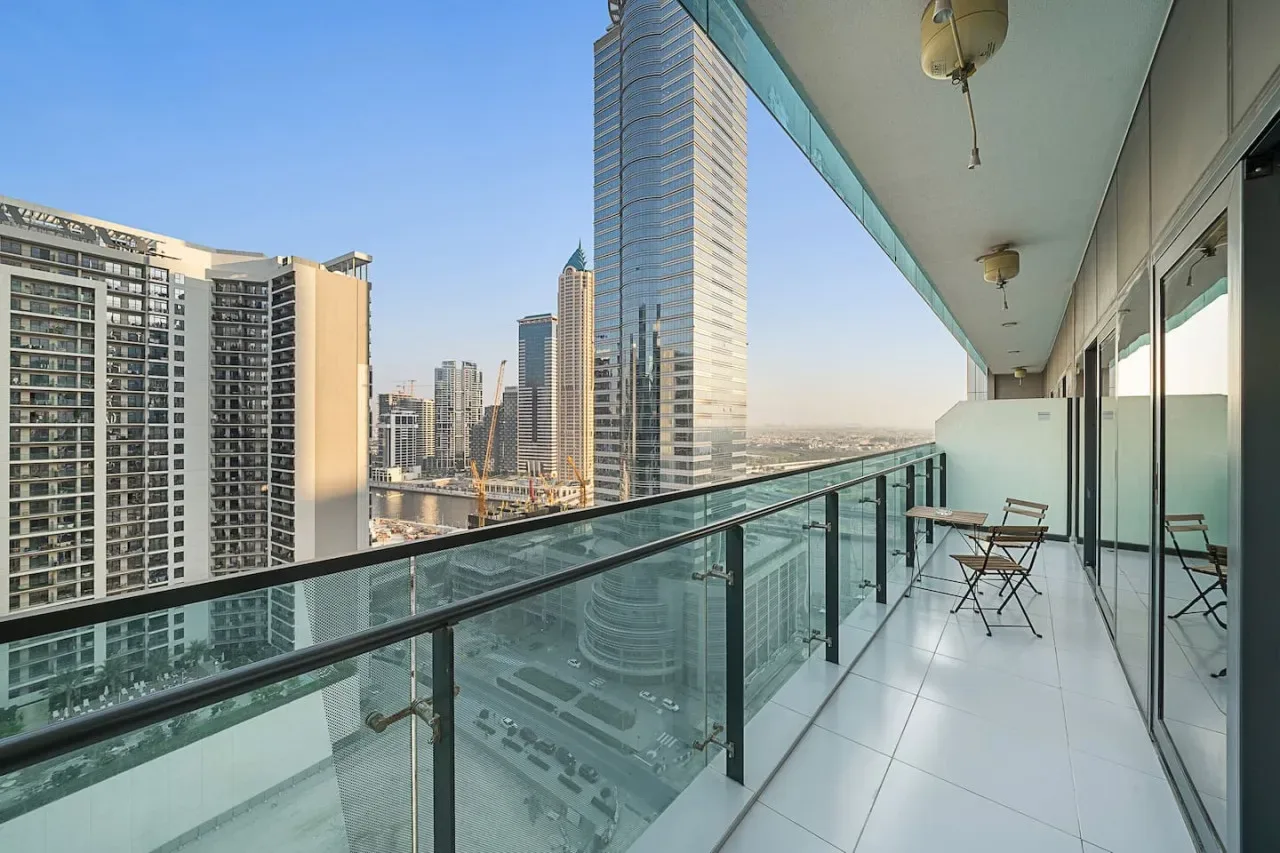 A balcony with glass railings and seating overlooks a cluster of high-rise buildings.