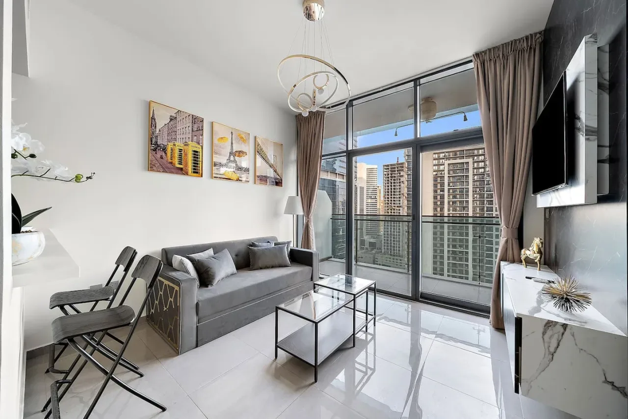 A bright living room with seating, a glass coffee table, and large windows.
