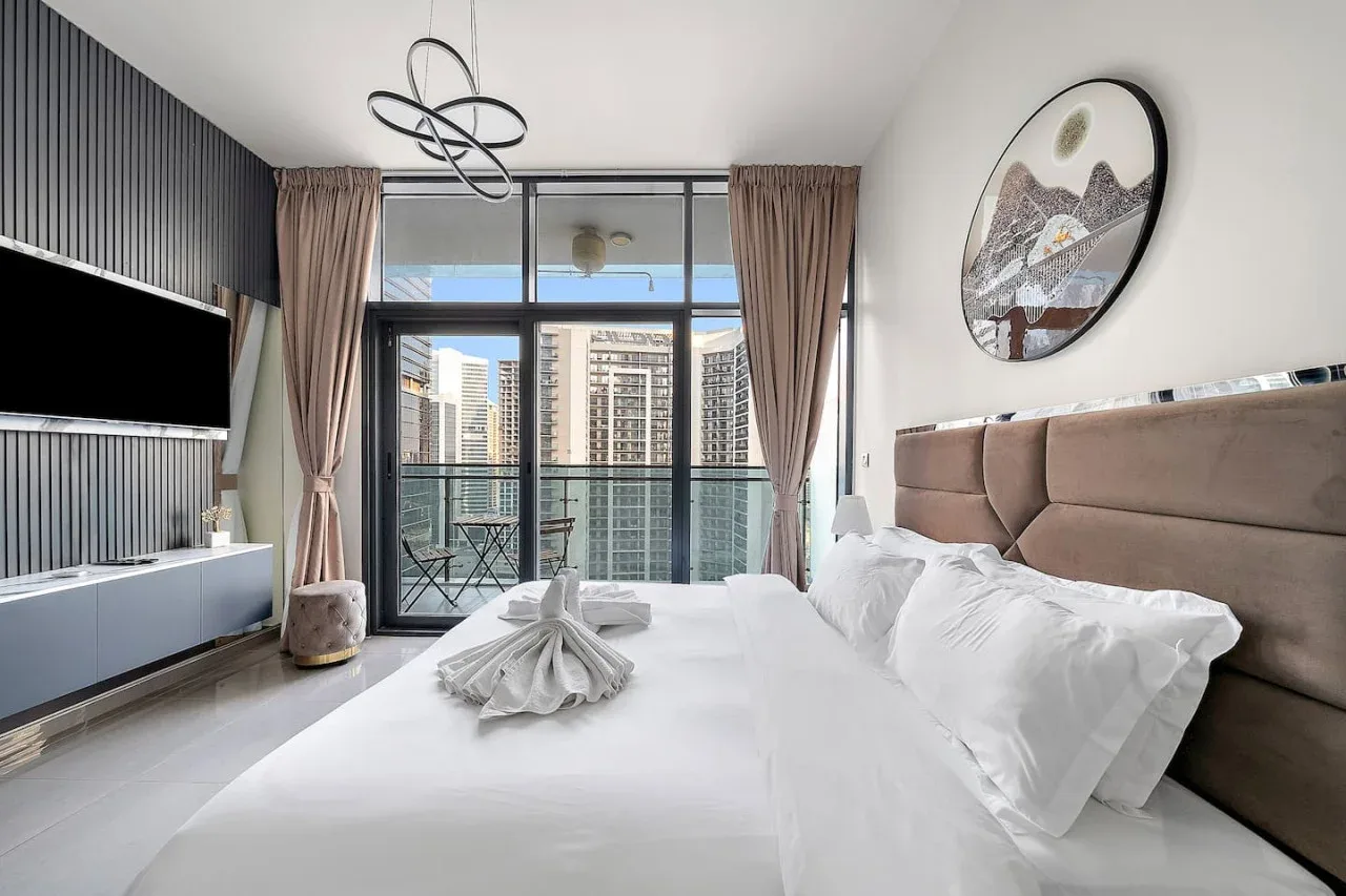 A bedroom with a neatly made bed and floor-to-ceiling windows.