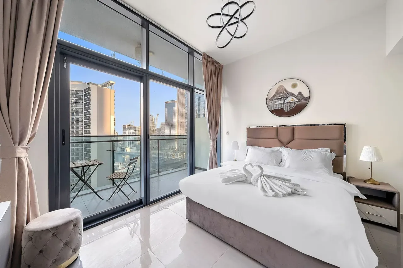 A bright bedroom with a large bed beside floor-to-ceiling windows.