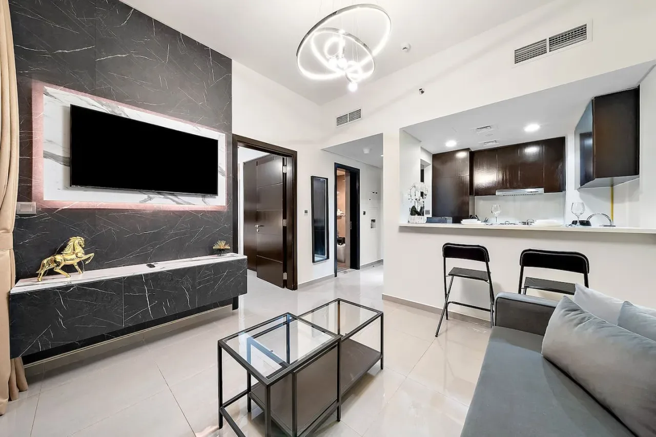 A modern living room with a wall-mounted television, glass coffee table, and open kitchen.