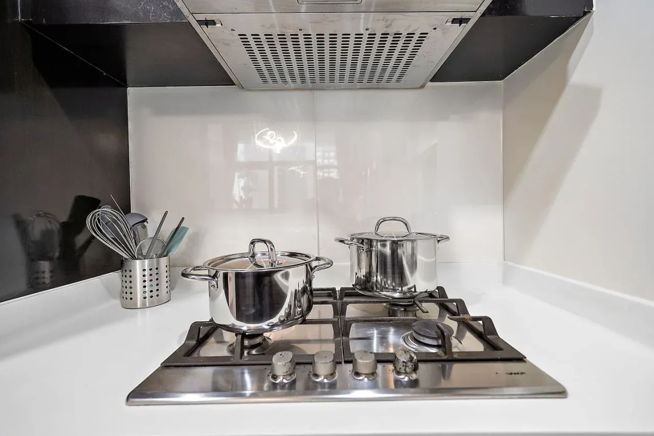 A kitchen stovetop holds two pots beside a container of cooking utensils.