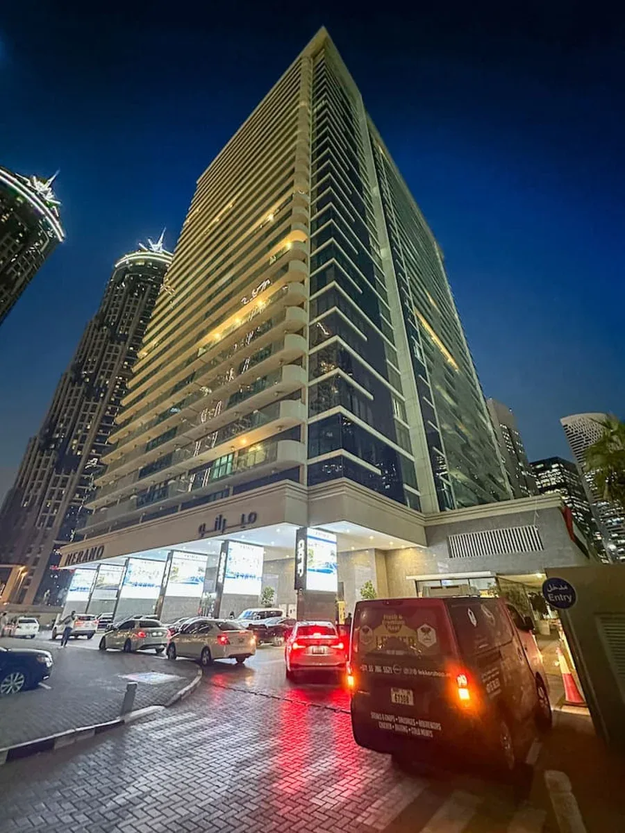 A tall illuminated high-rise building stands above a busy city street at night.