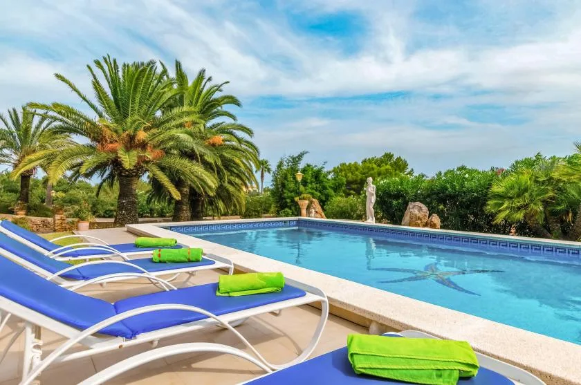 An outdoor swimming pool beside blue loungers and leafy palm trees.
