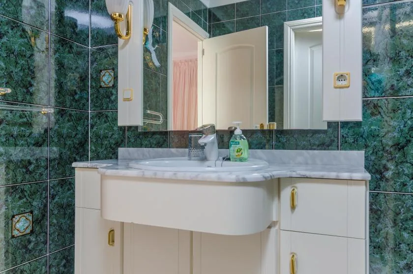 A bathroom vanity with a sink and mirror, set against green tiled walls.