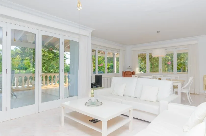 A bright living room with white seating and large windows overlooking greenery.