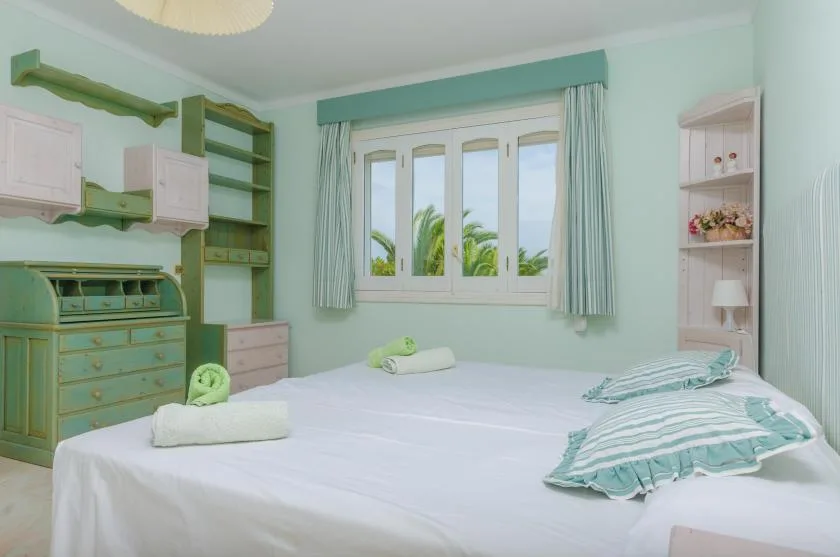 A bedroom with a bed, striped pillows, and a window overlooking palm trees.