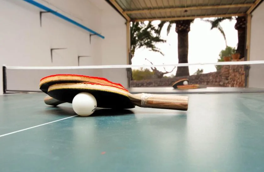 A table tennis setup with paddles and a ball rests on a green table.