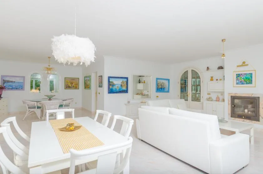 A bright living and dining area with white seating, a dining table, and colorful wall art.