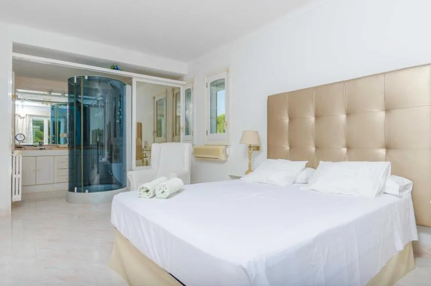 A bright bedroom with a large bed and a glass shower area.