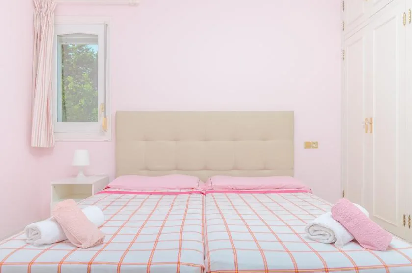 A pink bedroom with two beds and a window.