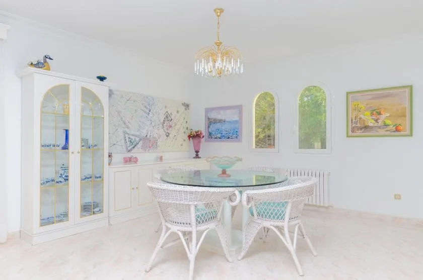 A bright dining room with a round table, wicker seating, and tall windows.