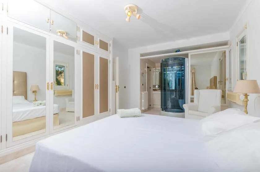 A bright bedroom with mirrored wardrobes and a glass shower in the background.