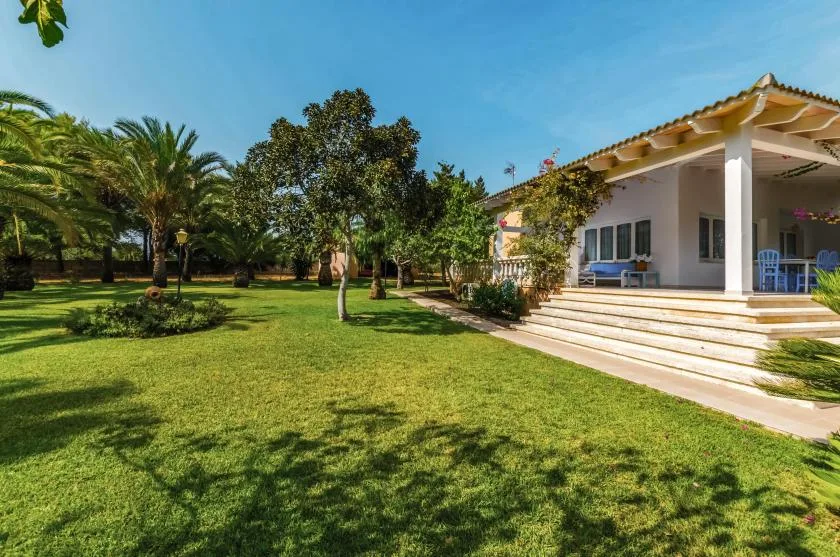 A grassy garden with trees beside a house with a covered patio.