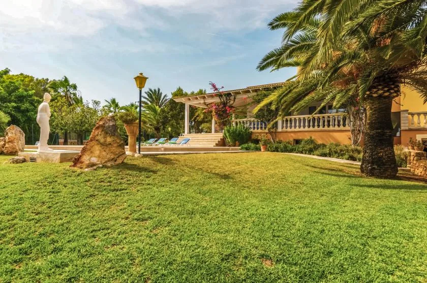 A landscaped garden with a statue, palm trees, and a covered terrace.